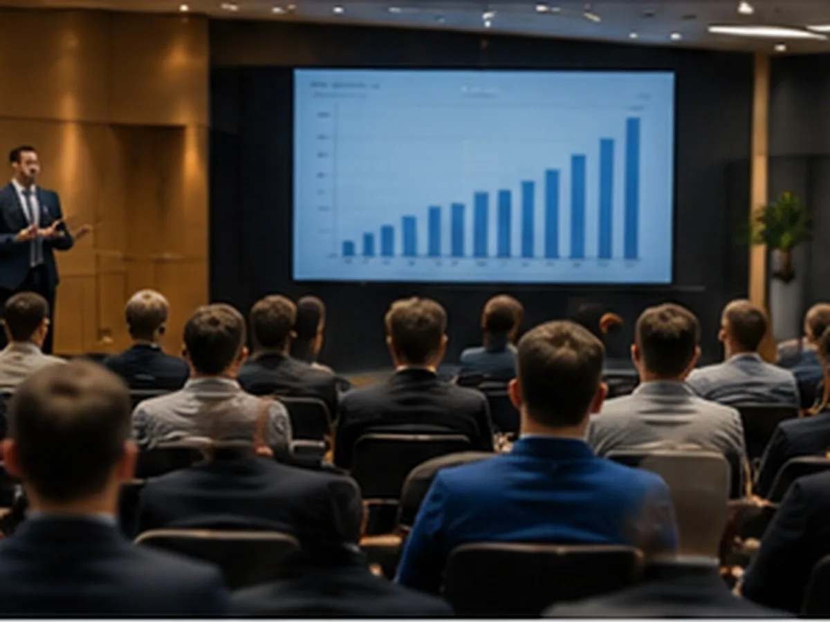 Auditório com pessoas sentadas assistindo a um apresentador ao lado de um telão com gráfico de barras crescente, ilustrando a assembleia de um grupo de consórcio em andamento